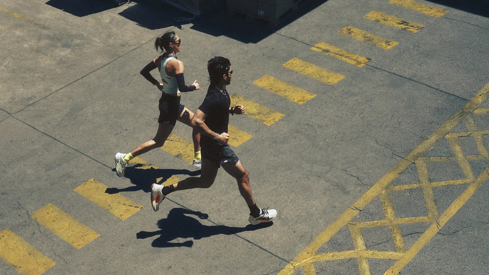 Due runner con scarpe HOKA Clifton Pro corrono su un piazzale industriale