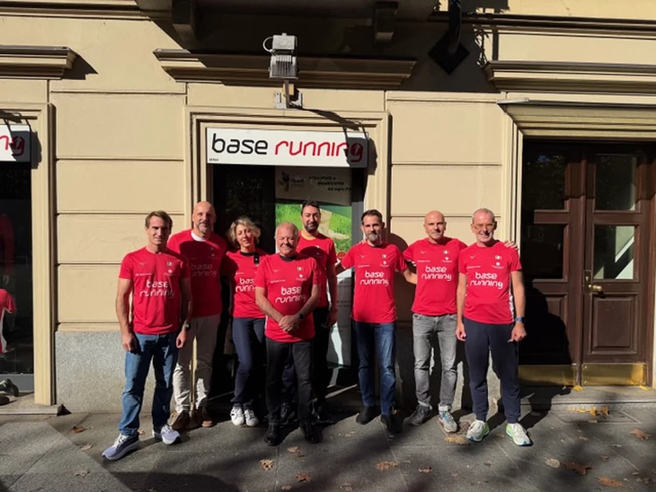 Base Running runners in the club’s red shirts outside the entrance with the Base Running sign in Turin, at their last meeting before leaving for New York